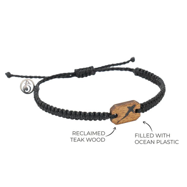 A black macrame bracelet with a small reclaimed teak wood charm decorated with a black shark filled with ocean microplastics.