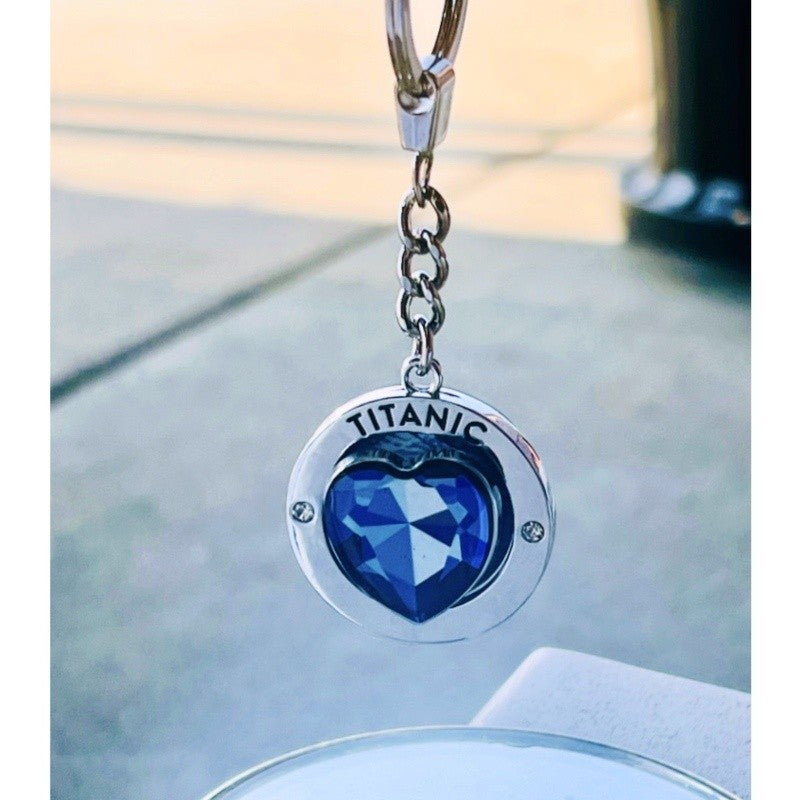 A disk-shaped key ring with spinning blue heart, shown hanging in natural light.
