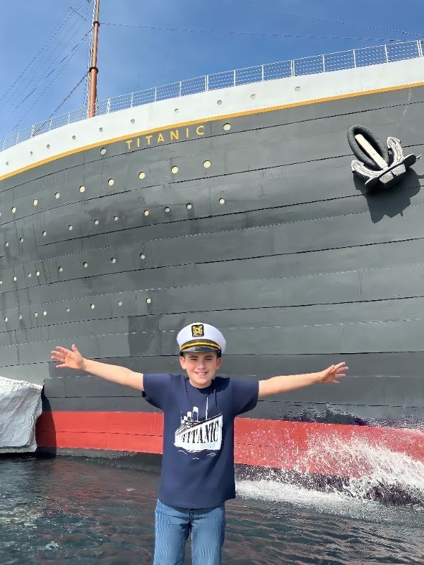A happy child wears a Captain Hat with arms stretched wide in front of the Titanic Museum Attraction.