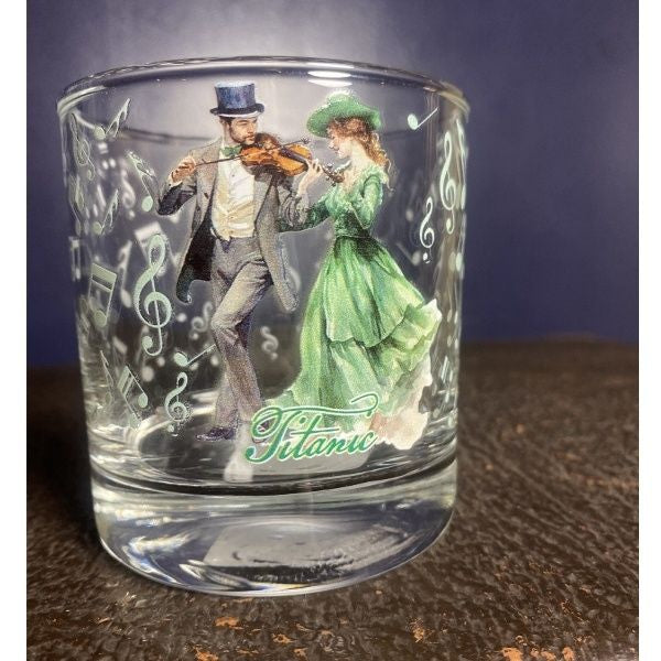 A clear old fashioned rocks glass printed with a happy Irish couple enjoying a merry fiddle tune surrounded by pale green music notes.