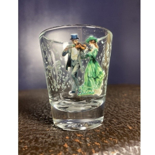 A clear standard shot glass printed with a coupe in formal attire enjoying a cheerful fiddle tune surrounded by pale green music notes.
