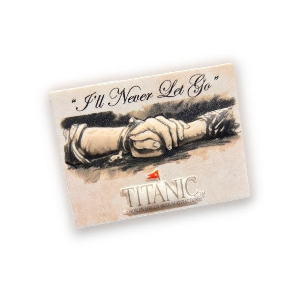 A miniature rectangular magnet, about the size of a USD quarter, with the words "'ll Never Let Go" above a sketch illustration of two clasped hands. Our Titanic logo is printed below. Plain white background.