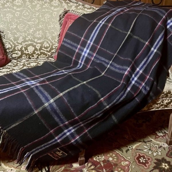 A black plaid narrow blanket with grey, gold, navy, and red stripes is laid out on a vintage couch.