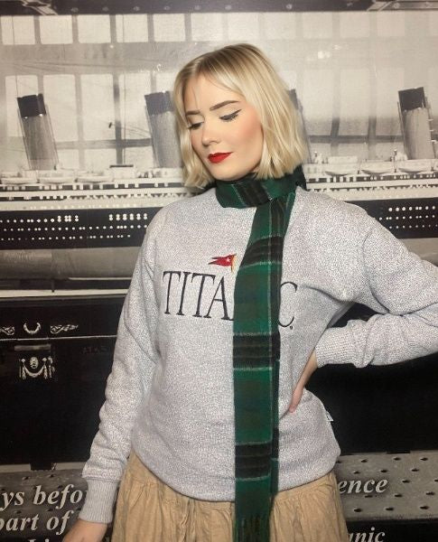 A woman poses while wearing a green tartan scarf.