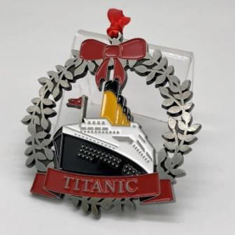A metal wreath detailed with red a enamel bow and banner encircle a vibrant enamel filled metal mold of the Titanic.