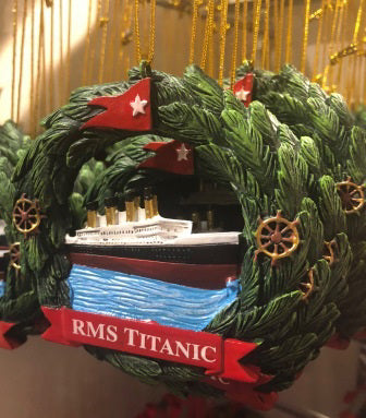 A hand painted molded wreath of decorated with ship's wheels and a red flag and banner encircle a painted Titanic at sea.