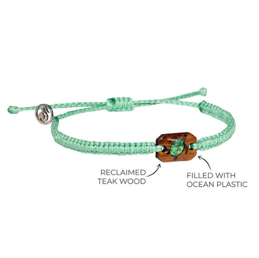A green macrame bracelet with a reclaimed teak wood charm decorated with a turtle shape filled with green microplastics recovered from the ocean.