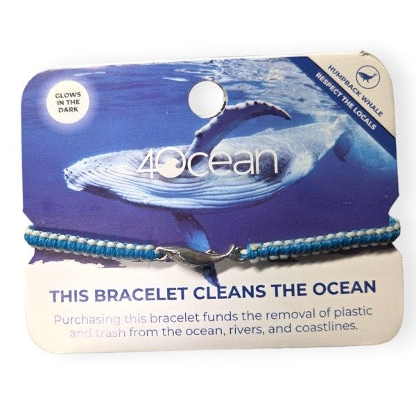 A macrame braided bracelet in sky blue with white glow accents and a humpback whale charm in silvery steel.