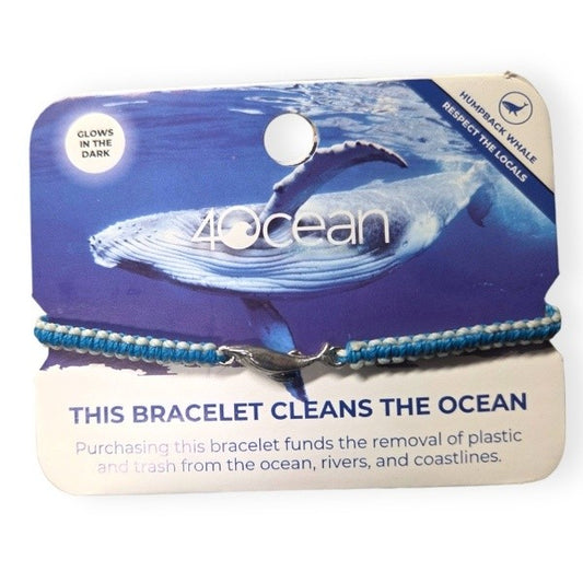 A macrame braided bracelet in sky blue with white glow accents and a humpback whale charm in silvery steel.