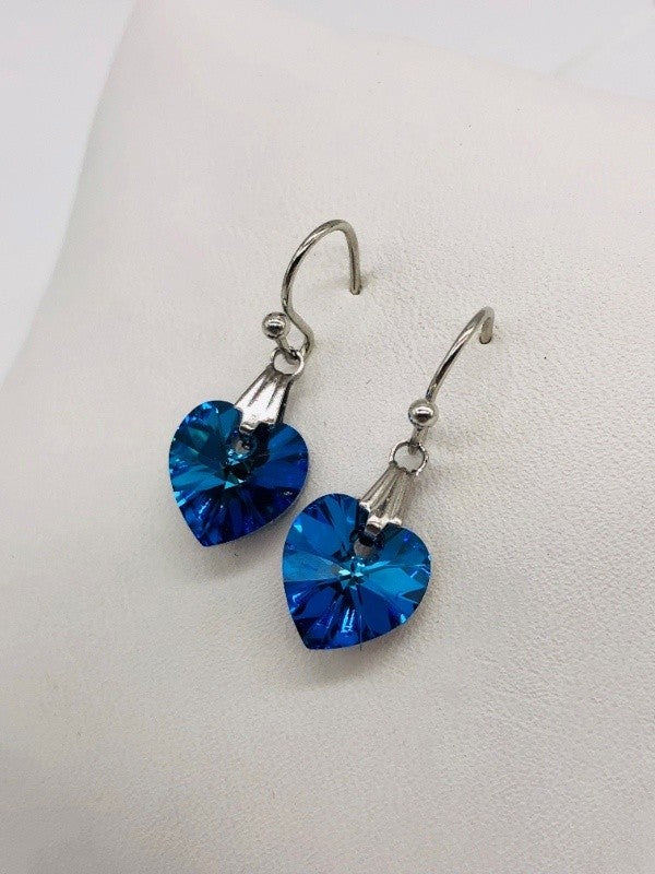 A pair of drop earrings. Light blue heart crystals dangle from silver hardware.