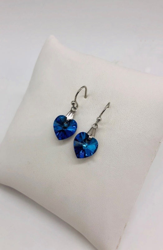 A pair of drop earrings. Light blue heart crystals dangle from silver hardware.
