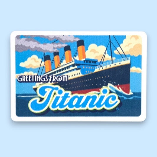 A rectangular white magnet printed with a vibrant illustration of the Titanic at sea with the text "Greetings From Titanic". The main color of the artwork is blue.