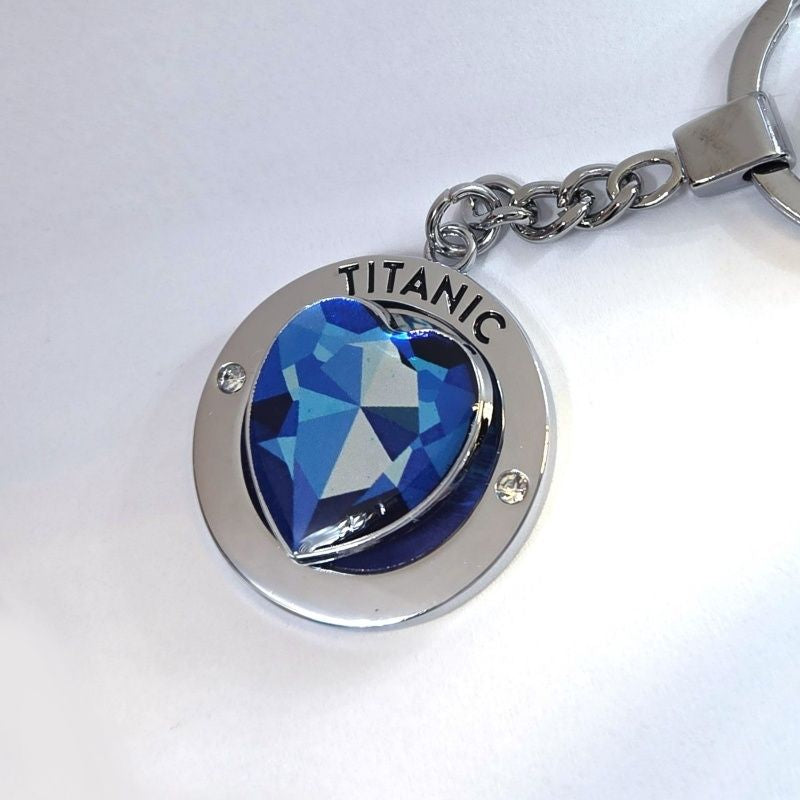A round silver tone key ring charm with a large heart printed to look like a blue diamond that spins. It says Titanic above the heart.