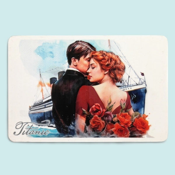 An elegantly dressed couple is shown in a close embrace from the waist up, roses and the Titanic ship frame them on this rectangular white magnet.