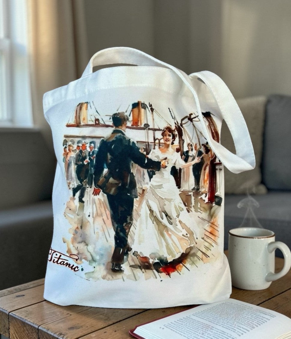 A white canvas tote bag with a happy couple dancing on Titanic's deck as a crowd cheers. The bag is displayed on a coffee table.