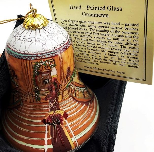 A painted glass bell shaped ornament with the Grand Staircase from Titanic decorated for Christmas. The cherub stands atop a burgundy gold bow, decorated garland lines the railing and center clock, and the milk glass dome tops off the arch of the bell.