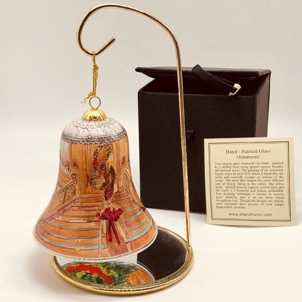 A view of the ornament displayed on a hanger with a mirrored base so you can see a hint of the inside reflected, in the background there is a black satin box and card telling how it was painted.