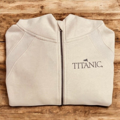 A light beige hoodie, folded, with a dark beige Titanic logo printed on one chest.