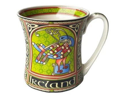 A white flared mug fully printed with a green, black, red, and blue design that depicts a stylized peacock made of Celtic knots.