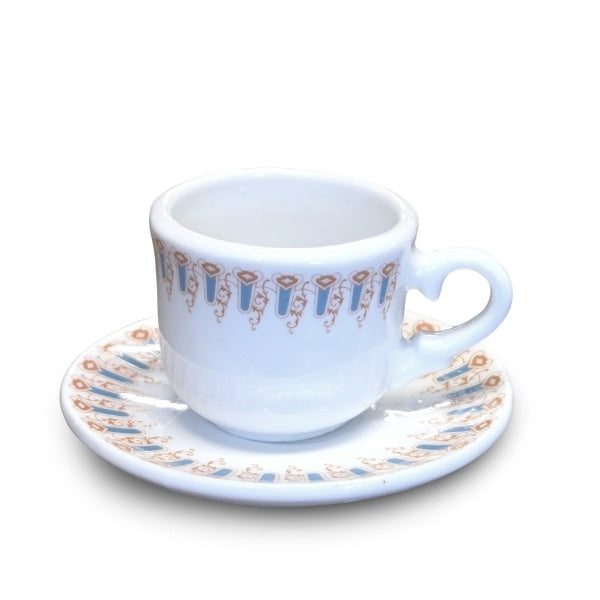A miniature white teacup with a light blue and brown swirling arches design around the rims, it is slightly smaller than a shot glass.