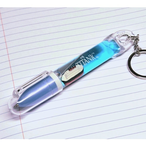 An aqua blue and clear pen with clear body and a small Titanic floating inside on top of blue water, displayed on lined notebook paper.
