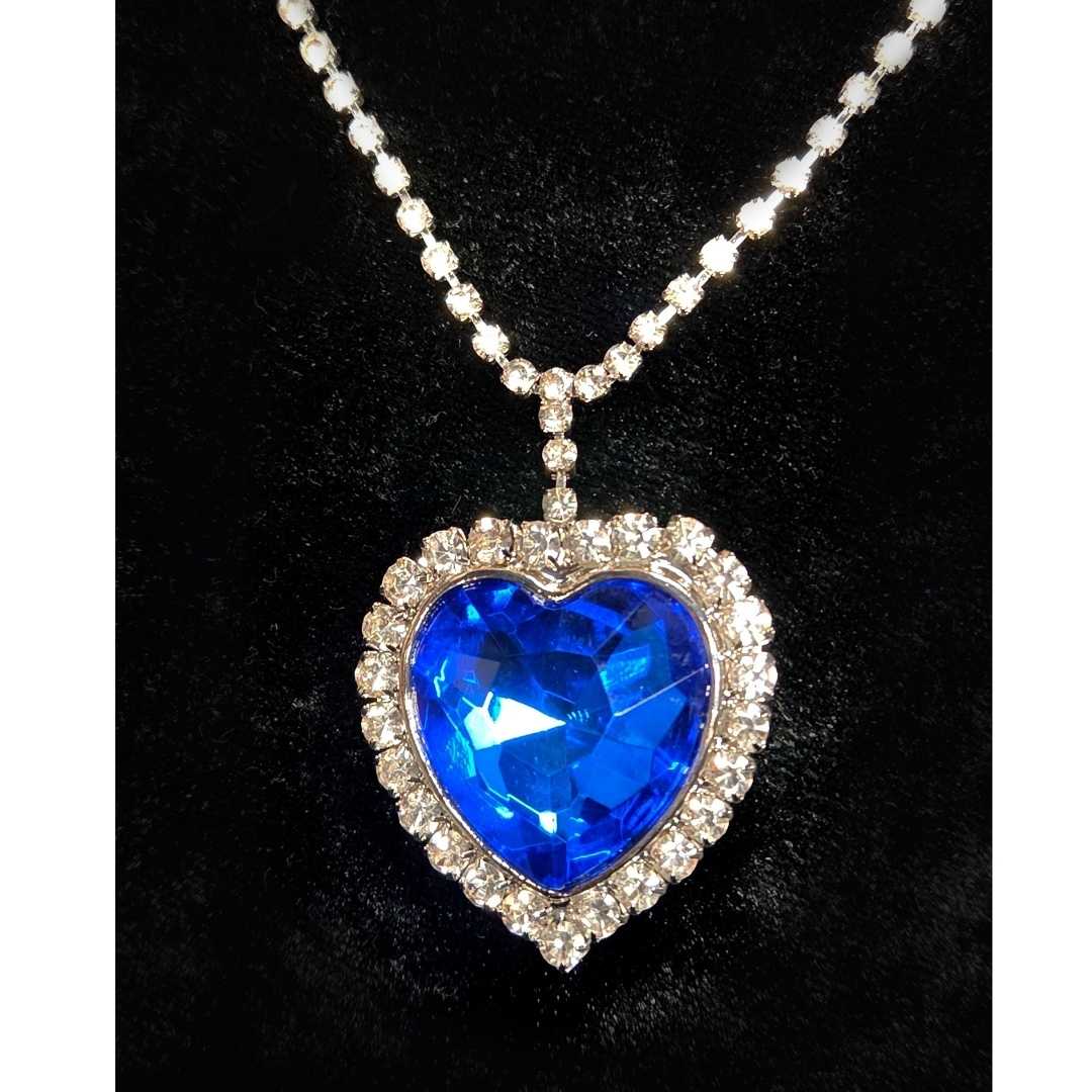 A large blue gem shaped like a heart is surrounded by chunky clear gems and hanging from a necklace made of smaller clear gems.