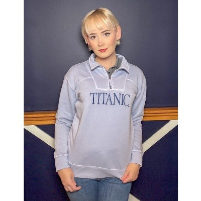 The same woman wearing the quarter zip pullover in muted pale blue with navy embroidery.