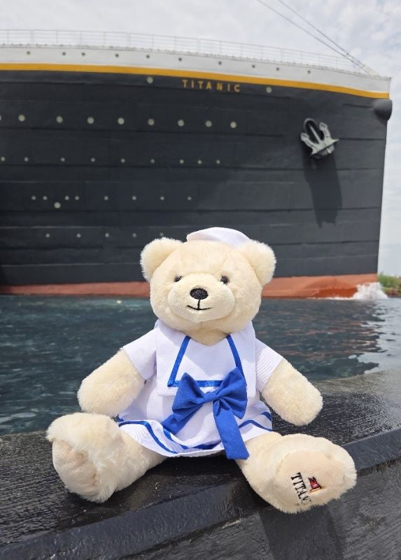 Polar bear plush in white and blue sailor dress next to Titanic ship.