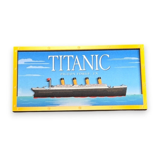 A rectangular magnet with two layers. The back layer displays a bright blue sky and the Titanic's name. The front layer features a raised image of the Titanic ship on water, and a yellow frame bordering the whole design.