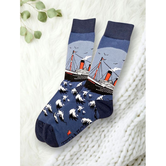 Titanic socks with several shades of blue. The ship is black and white with orange smokestacks and details. It is sailing across waves as birds fly in the distance overhead.