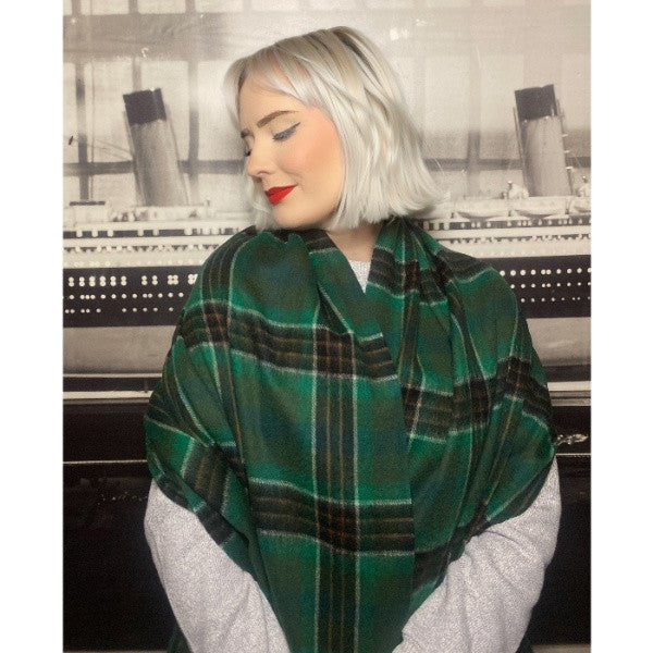 A woman looks looks to the side while wearing a green wool tartan stole wrapped around her shoulders - cozy and warm.