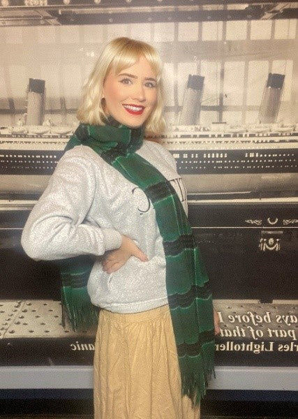 A woman wears her green tartan stole around her neck like a thick scarf.