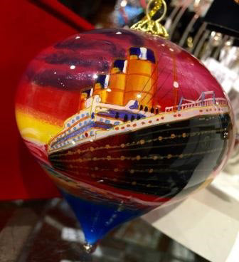 The Titanic is painted on a glossy teardrop shaped glass ornament in a vibrant sunset of reds and yellows.