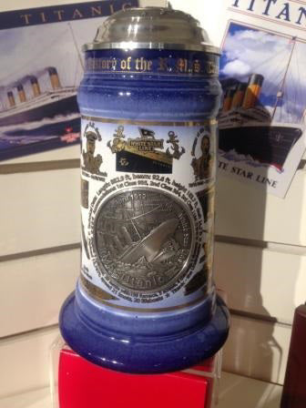 A large fancy stein with domed metal top and big pewter emblem of the Titanic sinking on the front. The stein is a blue and white fade accented with golden icons from the Titanic's history.