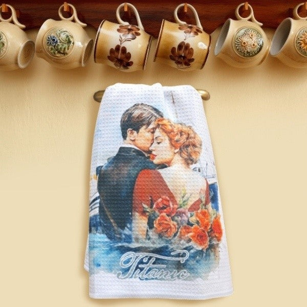 A dish towel featuring our embracing couple watercolor design, displayed on a small gold bar under a row of rustic hanging mugs.