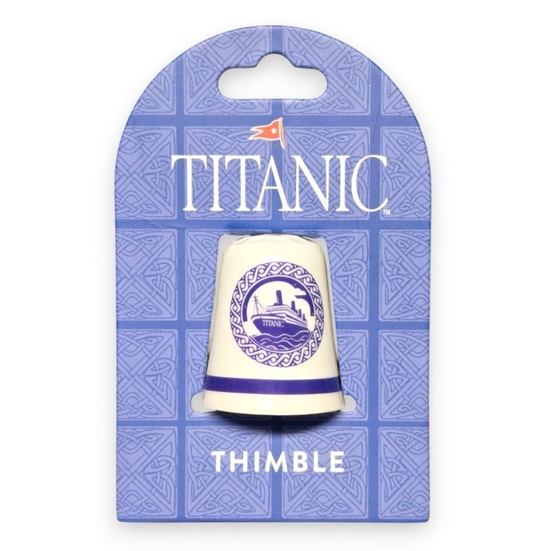 The Titanic Delft Thimble in its packaging, an arched heavy cardstock printed with delicate blue Celtic knots and our Titanic logo in white.