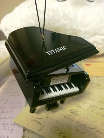 The Titanic's name is printed on top of the piano's lid, and the ornament hangs from the lid while staying propped open.