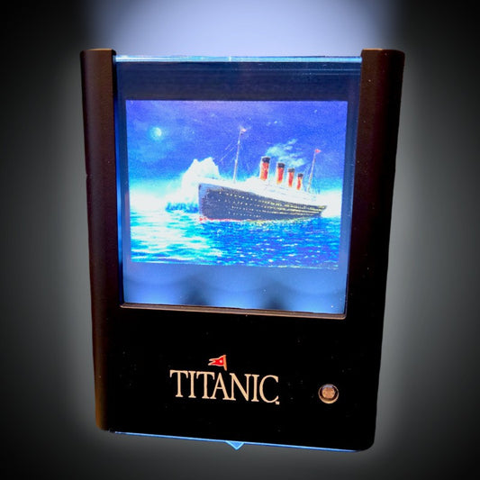 Titanic and iceberg picture illuminated in black plastic frame printed with ship's name. Product is displayed on an illustrated light to dark gradient.