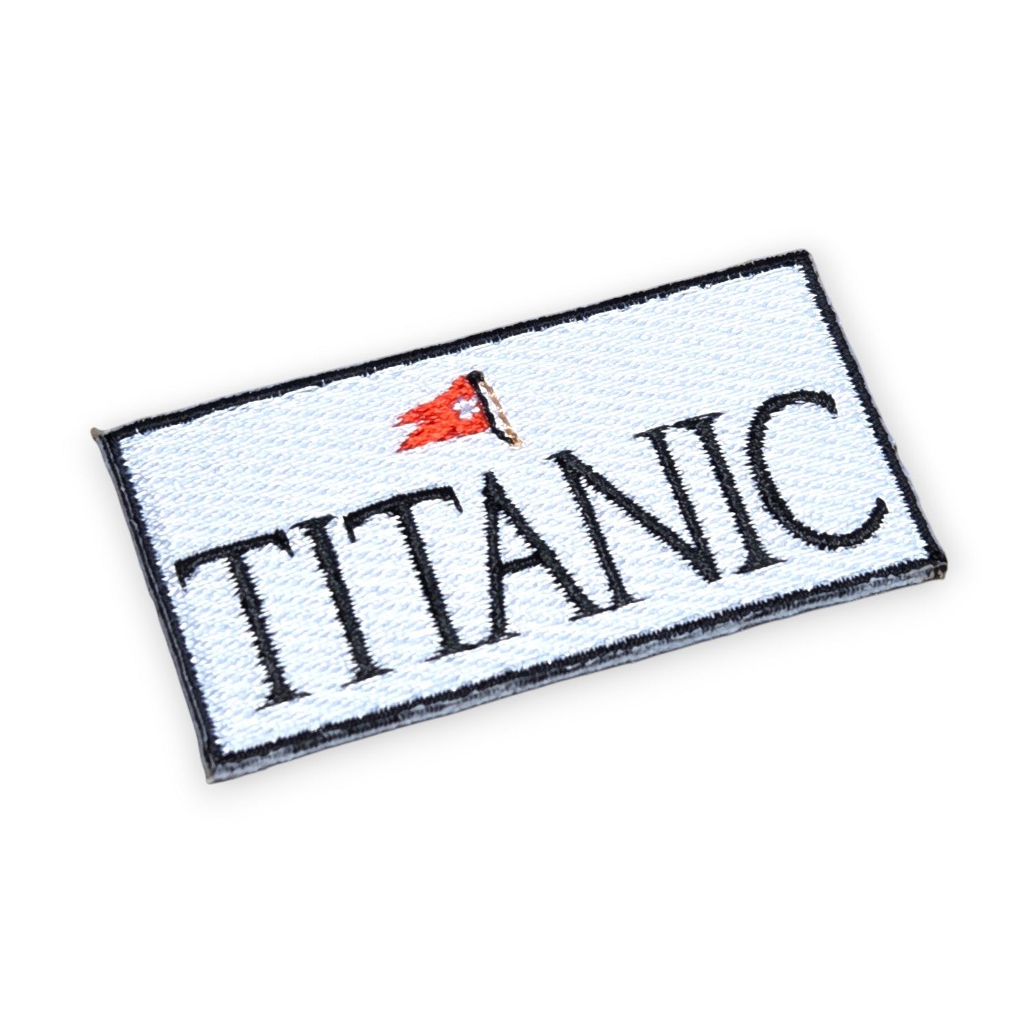 A small rectangular wide patch that says Titanic in all capital black letters on a solid white background with a narrow black border. A red white star line flag is embroidered above the ship's name.