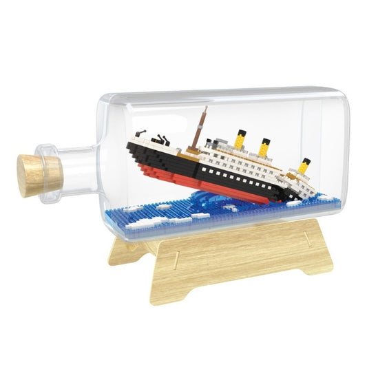 A building block kit of the Titanic breaking in half and sinking set inside a large acrylic bottle with cork, on a simple wooden base.