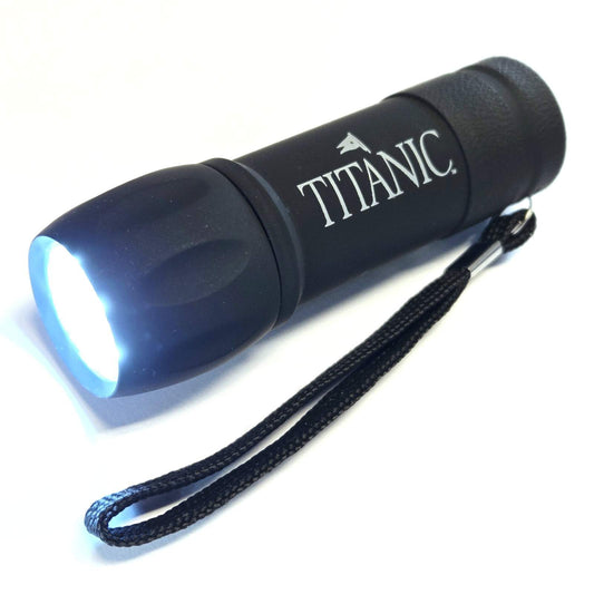 An illuminated black mini flashlight with white Titanic logo and attached loop strap.