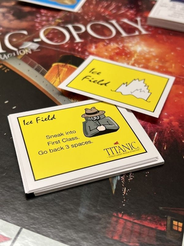 The yellow chance cards are called the Ice Field, the one on display shows an illustrated iceberg on the back and a cartoonish man in a trench coat and hat with the instructions "Sneak into First Class, go back 3 spaces."