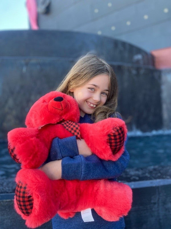 A young girl smiling as she gives a large red bear plush toy a big hug.