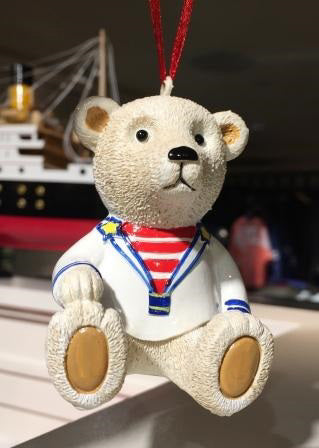 A sculpted polar teddy bear in a sailor uniform hangs from a red string as an ornament.