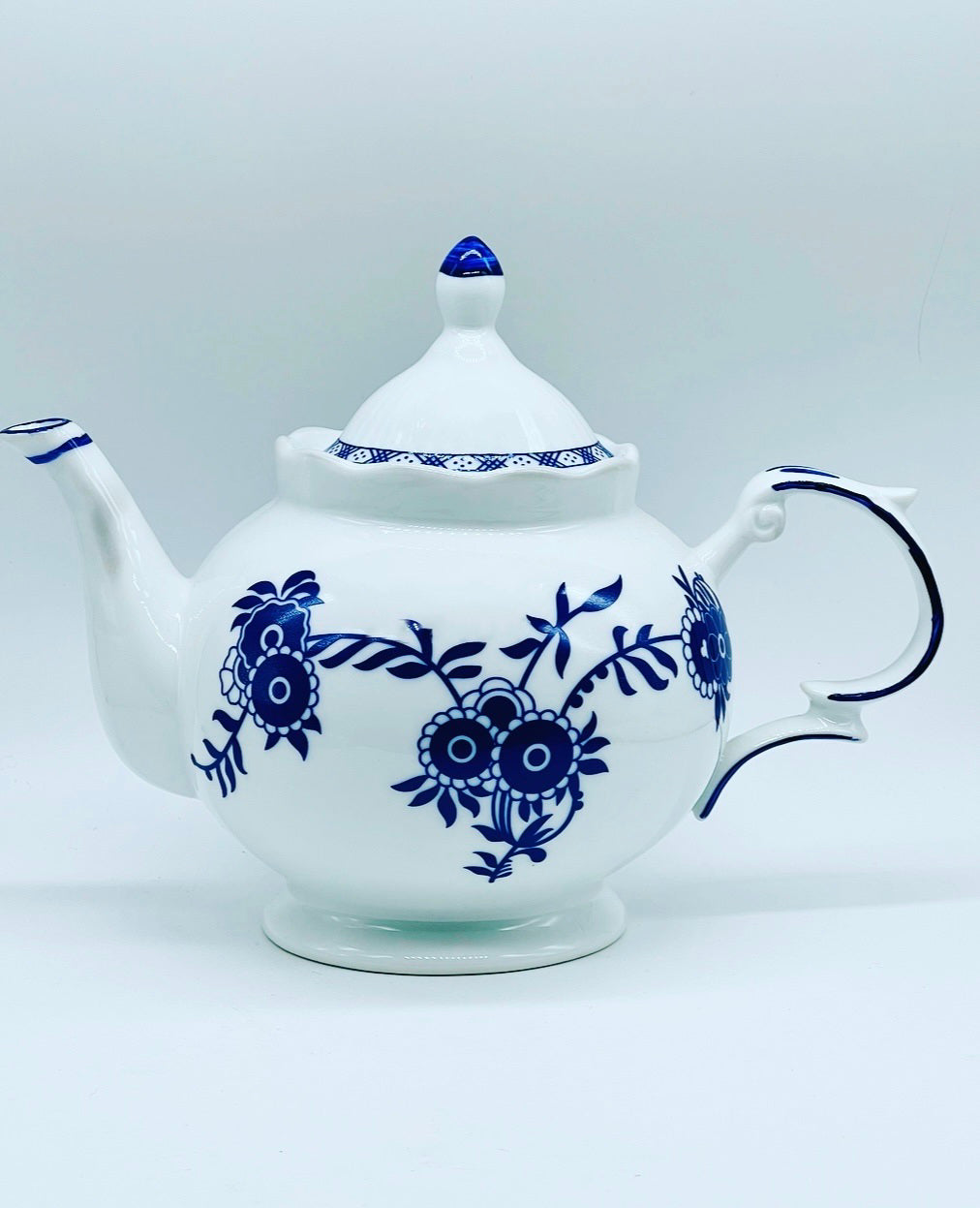 A white ceramic teapot decorated with a vintage blue delft flower pattern.