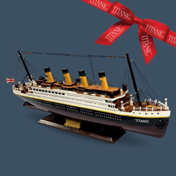 A highly detailed wooden Titanic model on a matching base. The backdrop is slate blue, and accented with a red Titanic ribbon.