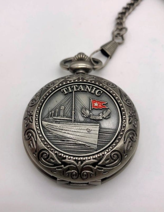 A dark silver-tone antique style pocket watch with swirling design on border and pewter emblem of the Titanic with a small red enamel nautical flag detail.