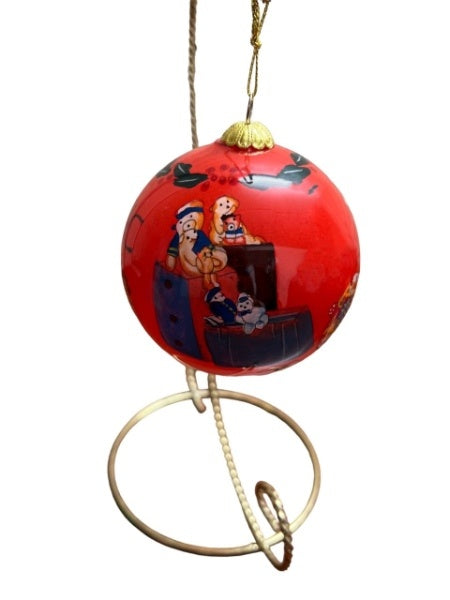 A red ball ornament depicting a hand painted pile of toys including plush polar bears and dogs painted atop luggage.